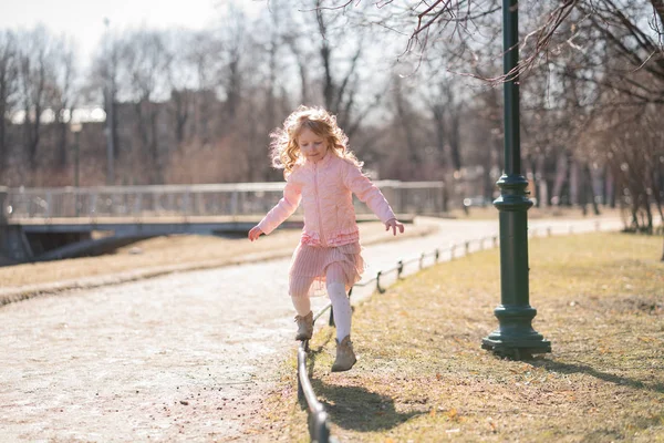 Menina muito feliz em casaco rosa, saia bonito e meia-calça quente vai no passeio no dia ensolarado no parque da cidade sozinho — Fotografia de Stock