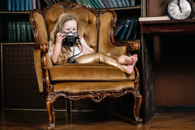 fotoğraf makinesi ile büyük altın rahat sandalyede oturan mutlu güzel küçük kız yatay fotoğraf