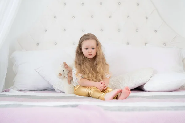 Retrato de uma menina triste com rosto infeliz sentado em uma cama no quarto — Fotografia de Stock
