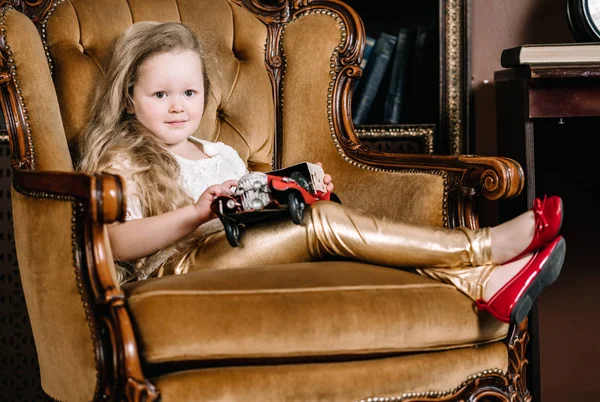 レトロな金色の椅子に座って、赤い車のヴィンテージのおもちゃで遊んで小さな女の赤ちゃんの女の子 — ストック写真