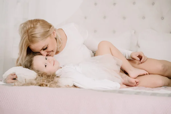 Porträt einer fröhlichen Mutter und ihrer Tochter, die sich am Bett vor weißem Hintergrund entspannen und freuen — Stockfoto