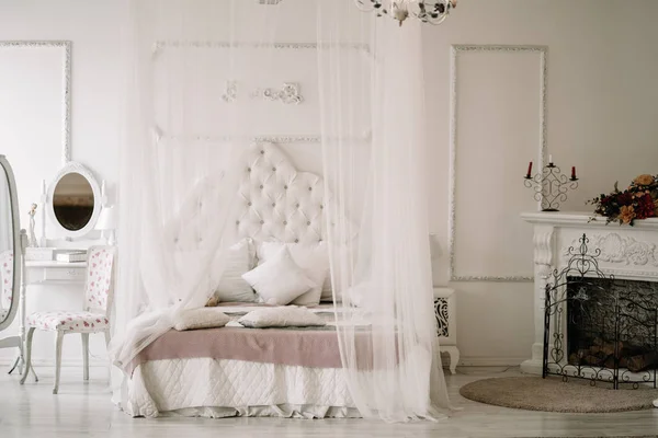 White bedroom interior with nobody. large cozy bed with a white canopy and oval dressing mirror with dressing table next to it