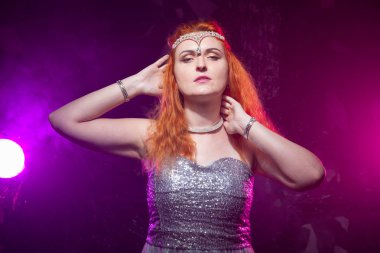 Olgun artı boyutu gri gece elbisesi içinde kırmızı saçlı kadın cadılar bayramı için hazır koyu duman arka plan üzerinde poz.