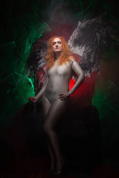 Mysterious plus size red hair girl in skincolor beige outfit with black and white big demon wings on gothic cemetery. Witch or dark angel style. Woman tempts by apple in the middle of the night — Stock Photo, Image