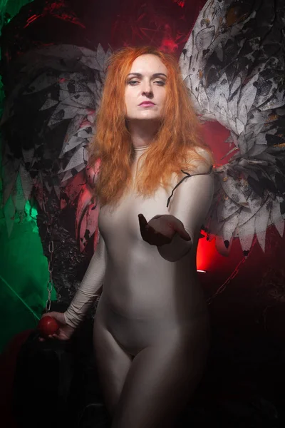Μυστηριώδες συν μέγεθος κόκκινο κορίτσι μαλλιά σε δέρμα μπεζ φόρεμα με μαύρες και λευκές μεγάλες δαίμονες φτερά στο γοτθικό νεκροταφείο. Μαγικό ή σκοτεινό άγγελο. Γυναίκα δελεάζει με μήλο στη μέση της νύχτας — Φωτογραφία Αρχείου