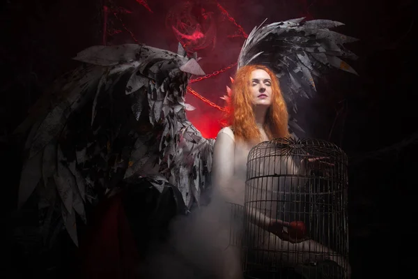 An evil tempting woman with large demon wings holds an Apple in a large cage and beckons to sin. Halloween photo plus size girl with red hair on a huge Gothic throne. — Stock Photo, Image