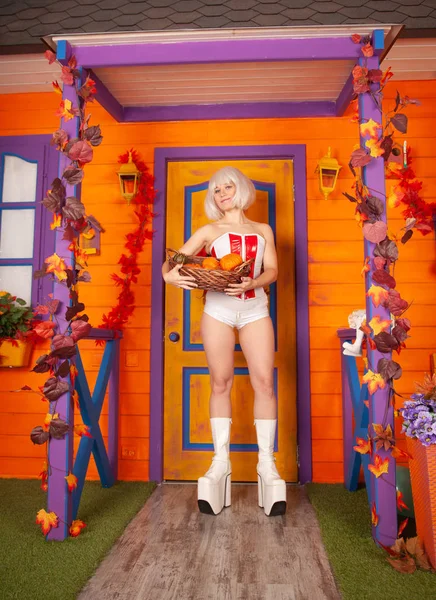 흰색 빨간 코르셋과 거대한 흰색 플랫폼 괴물 부츠에서 할로윈 파티를 준비하고 그녀의 오렌지 집 근처에서 포즈를 취하는 미래지향적 인 여성 — 스톡 사진