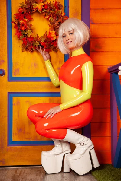 Hete mooie blonde vrouw in heldere kleurrijke latex rubber Catsuit klaar voor Halloween herfst feest en poseren in de buurt van haar oranje huis — Stockfoto