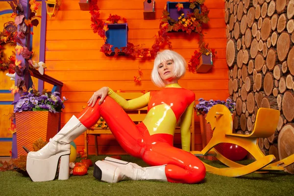 Hete mooie blonde vrouw in heldere kleurrijke latex rubber Catsuit klaar voor Halloween herfst feest en poseren in de buurt van haar oranje huis — Stockfoto