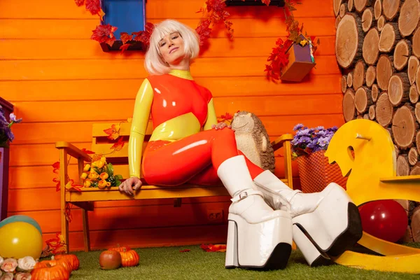 Hete mooie blonde vrouw in heldere kleurrijke latex rubber Catsuit klaar voor Halloween herfst feest en poseren in de buurt van haar oranje huis — Stockfoto