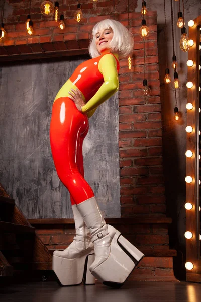 Hot High Fashion vrouw in helder oranje met Lime groen rubber outfit. mooie futuristische vrouw in strakke latex Catsuit poseren alleen thuis. — Stockfoto