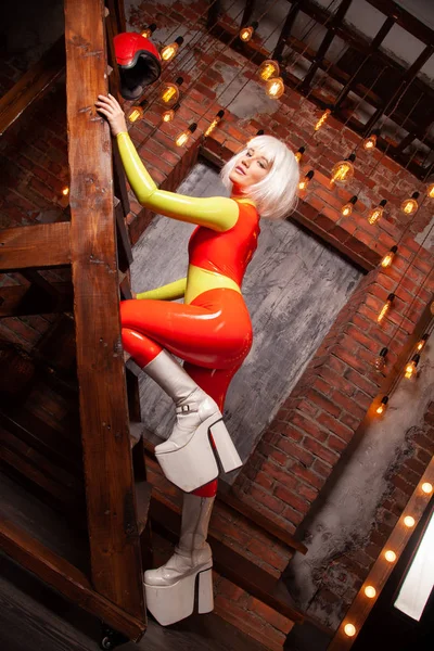 Hot high fashion female in bright orange with lime green rubber outfit. beautiful futuristic woman in tight latex catsuit posing alone at home. — Stock Photo, Image