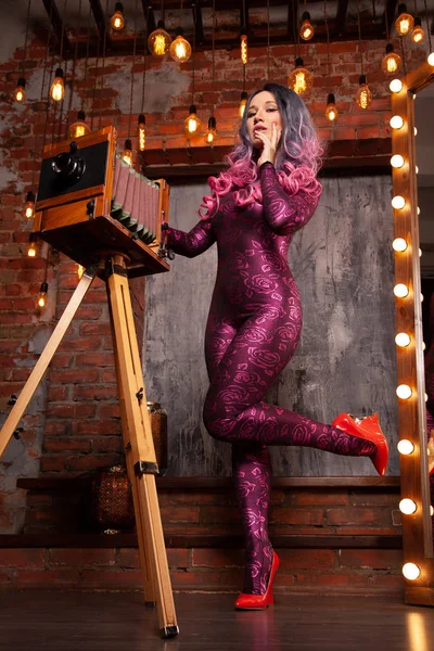 Charmante Luxus modische Frau in einem engen Sprunganzug mit einer großen Retro-Kamera posiert und Fotos zwischen den hellen Glühbirnen — Stockfoto