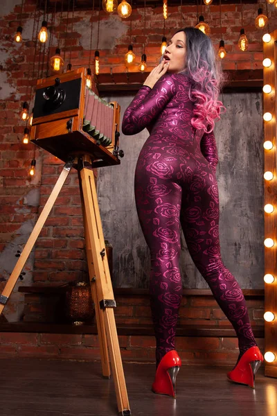 Charmante Luxus modische Frau in einem engen Sprunganzug mit einer großen Retro-Kamera posiert und Fotos zwischen den hellen Glühbirnen — Stockfoto