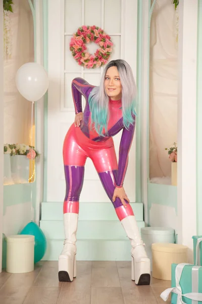 Jolie fille adulte mignonne en costume de caoutchouc de latex violet posant près de la boutique de cadeaux avec des cadeaux et des ballons à air. femme fétiche en tenue serrée posant seule. portrait pleine longueur . — Photo