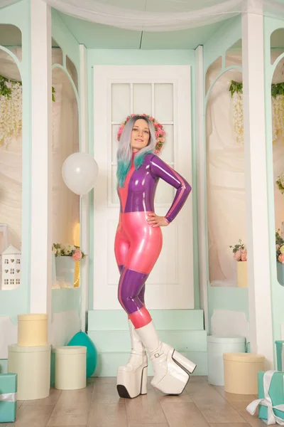 Vrij schattig volwassen meisje in paars latex rubber kostuum poseren in de buurt van cadeauwinkel met cadeautjes en luchtballonnen. fetisj vrouw in strakke outfit poseren alleen. volledige lengte portret. — Stockfoto