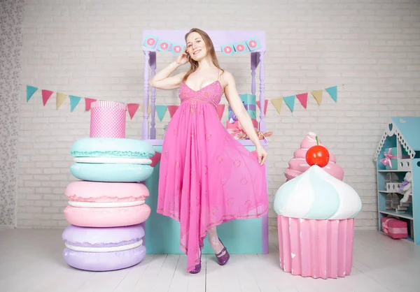 Милий щасливий дорослий дівчина позує в модній сукні серед величезних казкових цукерок і тортів — стокове фото