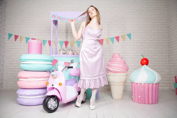Linda chica adulta feliz posando en vestido de moda entre enormes dulces y pasteles fabulosos —  Fotos de Stock