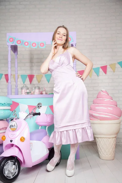 Schattig gelukkig volwassen meisje poseren in modieuze jurk onder enorme fabelachtige snoep en gebak — Stockfoto