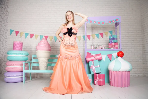 Милая счастливая взрослая девушка позирует в модном платье среди огромных сказочных сладостей и тортов — стоковое фото
