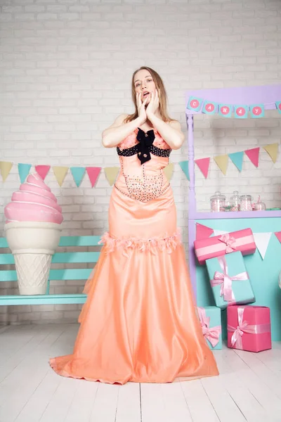 可愛いです幸せな大人の女の子のポーズでファッショナブルなドレスの間で巨大な素晴らしいお菓子やケーキ — ストック写真