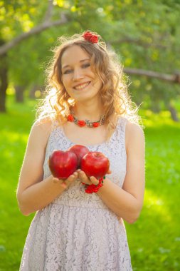 Güzel, güneşli bir yaz gününde elma bahçesinde yürüyen beyaz benekli elbiseli genç bir kadın.