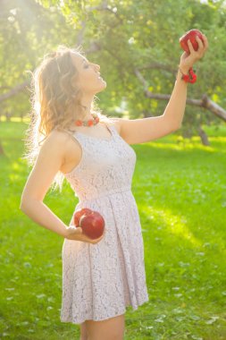 Güzel, güneşli bir yaz gününde elma bahçesinde yürüyen beyaz benekli elbiseli genç bir kadın.