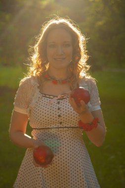 Güzel, güneşli bir yaz gününde elma bahçesinde yürüyen beyaz benekli elbiseli genç bir kadın.