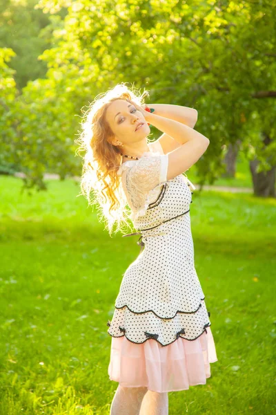 Jovem mulher em branco bonito polka dot vestido andando em um jardim de maçã em um lindo dia ensolarado de verão — Fotografia de Stock