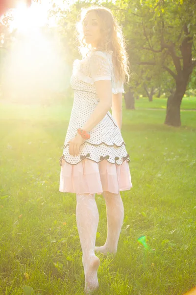 Jovem mulher em branco bonito polka dot vestido andando em um jardim de maçã em um lindo dia ensolarado de verão — Fotografia de Stock