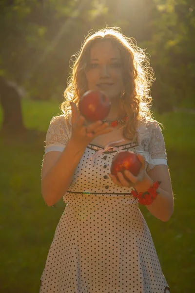Güzel, güneşli bir yaz gününde elma bahçesinde yürüyen beyaz benekli elbiseli genç bir kadın. — Stok fotoğraf