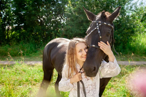 Hermosa chica joven caucásica caminando con un caballo y disfruta del verano en el campo . —  Fotos de Stock