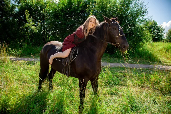 Hermosa chica joven caucásica caminando con un caballo y disfruta del verano en el campo . — Foto de Stock