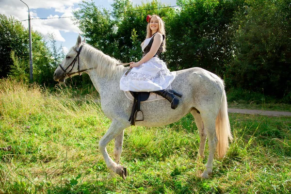 Όμορφη καυκάσια νεαρή κοπέλα με τα πόδια με ένα άλογο και απολαμβάνει το καλοκαίρι στην ύπαιθρο. — Φωτογραφία Αρχείου