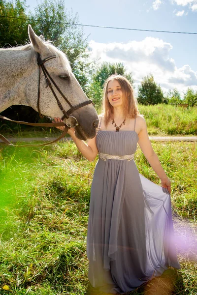 Belle jeune fille caucasienne marchant avec un cheval et profite de l'été dans la campagne . — Photo