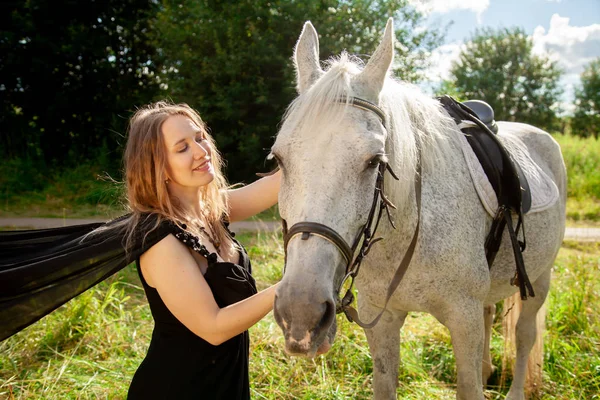 Belle jeune fille caucasienne marchant avec un cheval et profite de l'été dans la campagne . — Photo