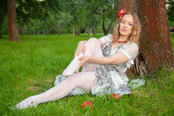 Menina na moda jovem em vestido de verão branco e meias de renda sentado na grama de verão à noite — Fotografia de Stock