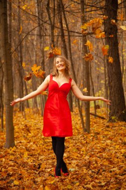 Kırmızı elbiseli bir kız sonbahar parkına yaprak atıyor.