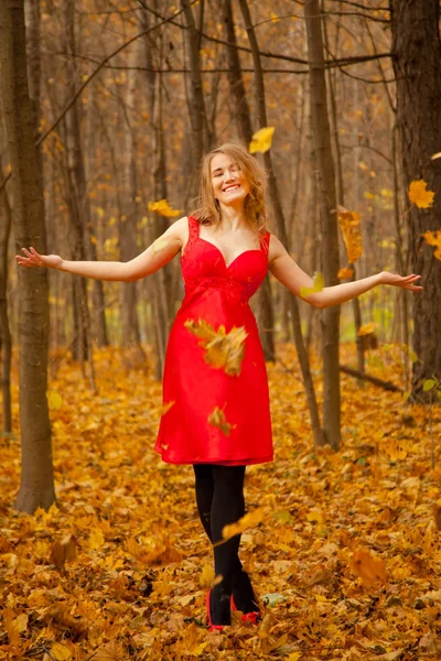 Uma menina em um vestido vermelho joga folhas em um parque de outono sozinho — Fotografia de Stock