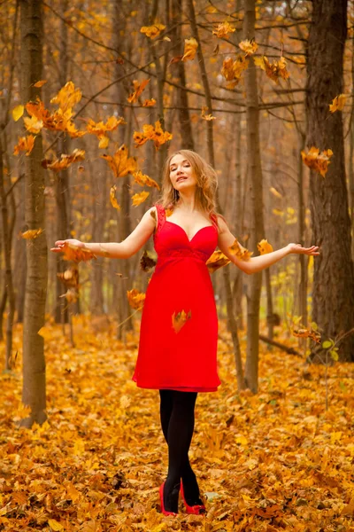 Uma menina em um vestido vermelho joga folhas em um parque de outono sozinho — Fotografia de Stock