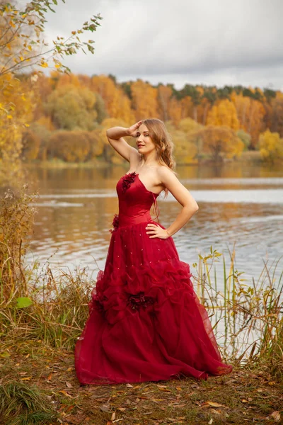 Jovem mulher em vestido de noite longa posando perto do lago no jardim de outono fundo sozinho — Fotografia de Stock