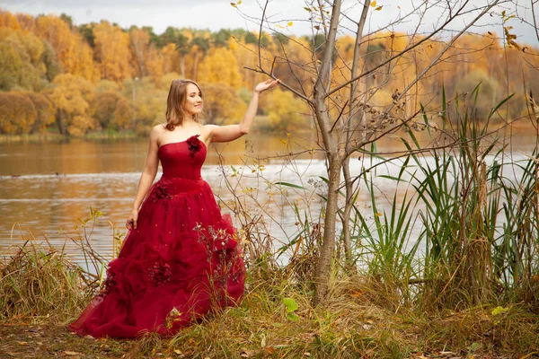 Junge Frau im langen Abendkleid posiert allein am See im herbstlichen Gartenhintergrund — Stockfoto