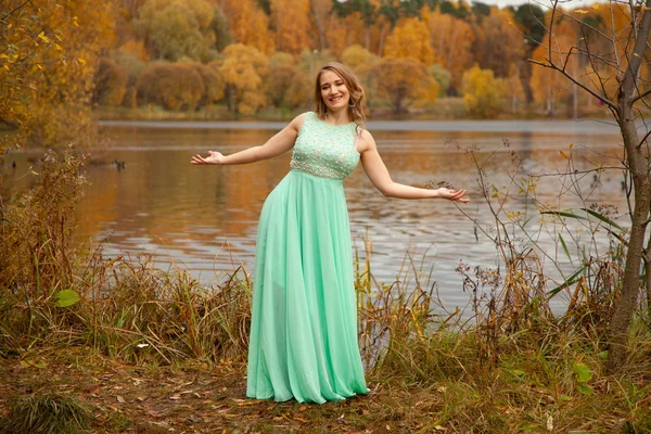 Junge Frau in mintblauem langen Kleid steht allein am Wasser im herbstlichen Gartenhintergrund — Stockfoto