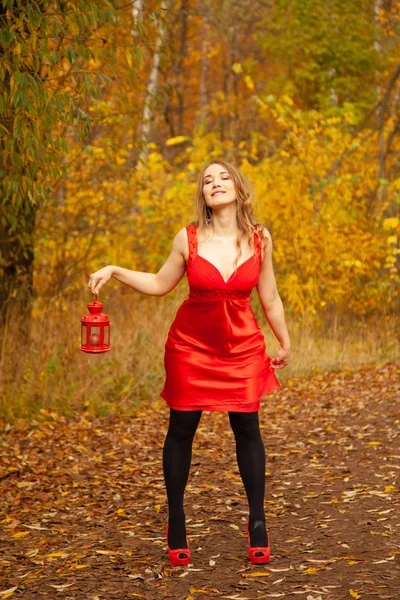 Chica caucásica en un vestido rojo camina con una luz retro en el parque de otoño solo entre el follaje colorido — Foto de Stock