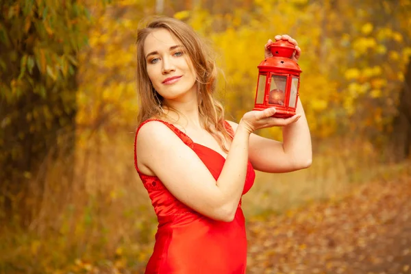 Chica caucásica en un vestido rojo camina con una luz retro en el parque de otoño solo entre el follaje colorido — Foto de Stock