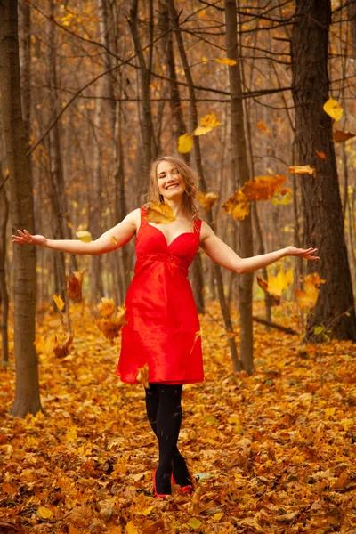 Uma menina em um vestido vermelho joga folhas em um parque de outono sozinho — Fotografia de Stock