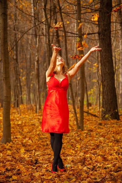 Ein Mädchen im roten Kleid wirft allein im herbstlichen Park mit Blättern — Stockfoto