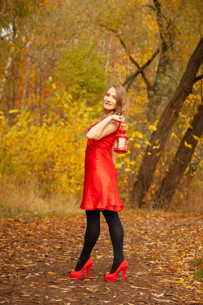 Menina caucasiana em um vestido vermelho caminha com uma luz retro no outono Parque sozinho entre a folhagem colorida — Fotografia de Stock