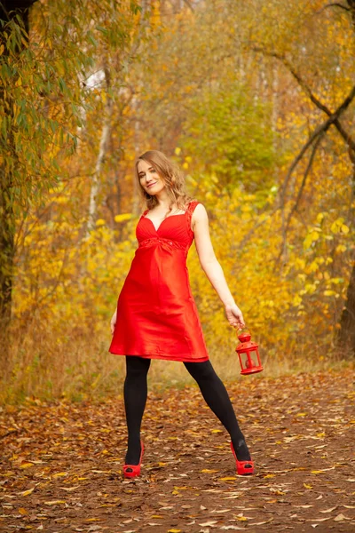 Kırmızı elbiseli beyaz bir kız sonbahar parkında geriye dönük bir ışıkla renkli yaprakların arasında yürür. — Stok fotoğraf