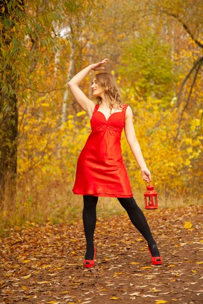 Menina caucasiana em um vestido vermelho caminha com uma luz retro no outono Parque sozinho entre a folhagem colorida — Fotografia de Stock